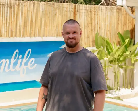 Nico, Gründer von Dreamlife.now, steht lächelnd vor der Dreamlife-Wandmalerei am Pool