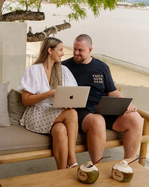 Nico, Gründer von Dreamlife.now, und Viktoria, Mitgründerin, arbeiten mit ihren Laptops auf einem Sofa am Wasser