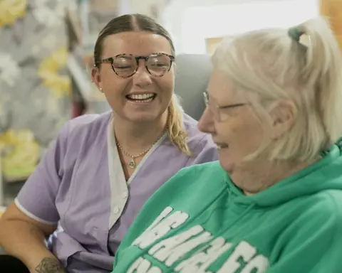 Pflegekraft lacht gemeinsam mit einer Seniorin